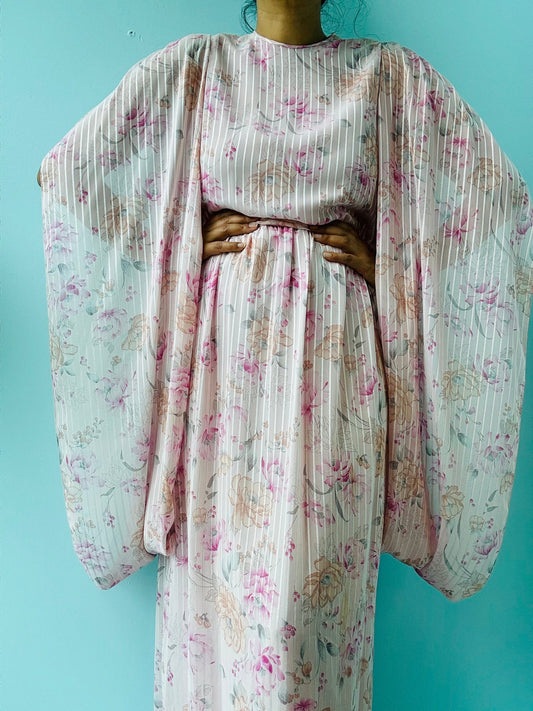 May include: A pink and white floral maxi dress with long sleeves and a gathered waist. The dress has a striped pattern and a delicate floral print.
